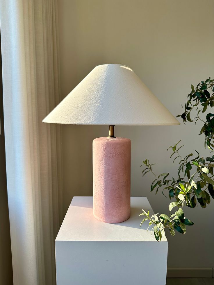 a pink lamp sitting on top of a white table next to a potted plant