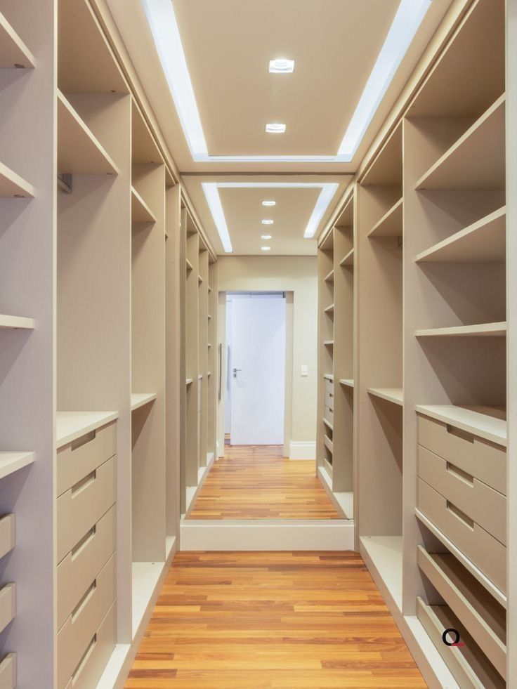 an empty walk - in closet with wooden flooring and white shelving units on both sides