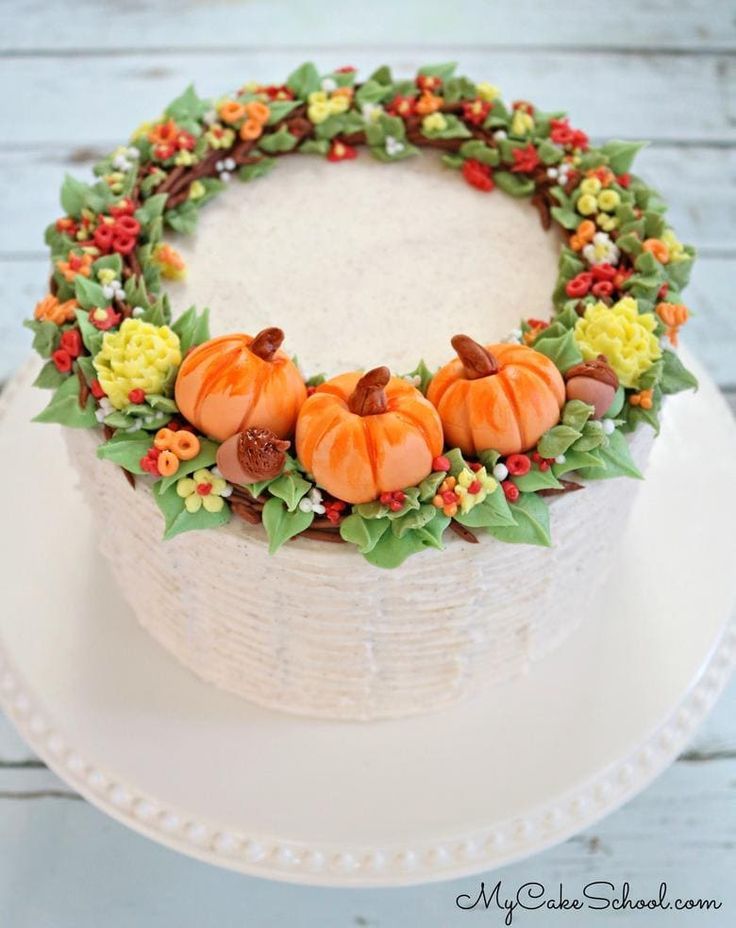 a cake decorated with pumpkins and flowers on a white platter next to a wooden table