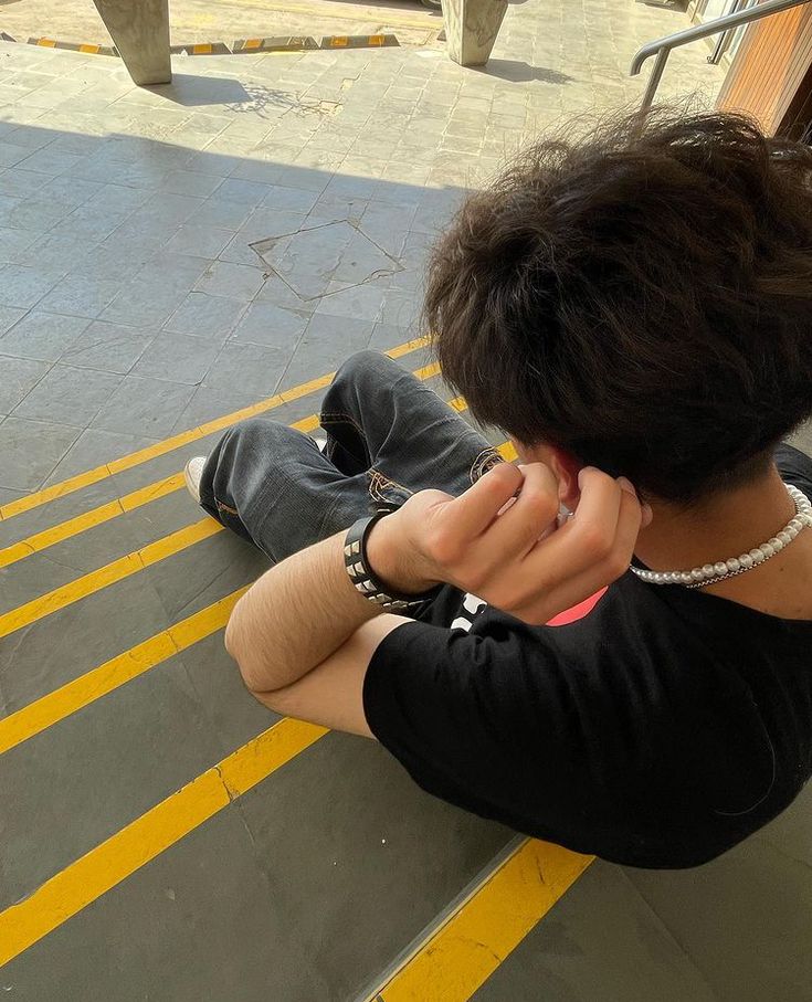 a person sitting on the ground with their hands to their ear and one hand near their face