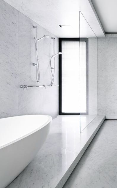 a white bathtub sitting next to a window in a bathroom with marble floors and walls