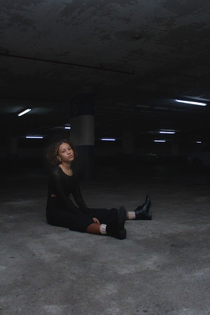 a woman is sitting on the floor in an empty parking garage with her eyes closed