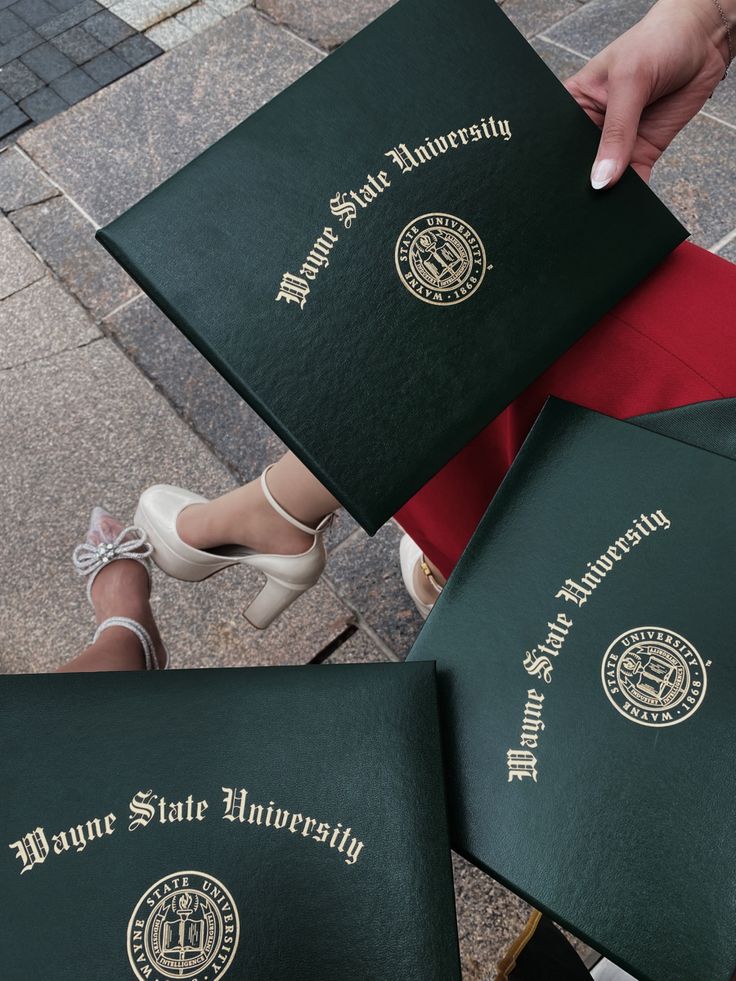 three green university diplomas sitting on top of each other in front of a building