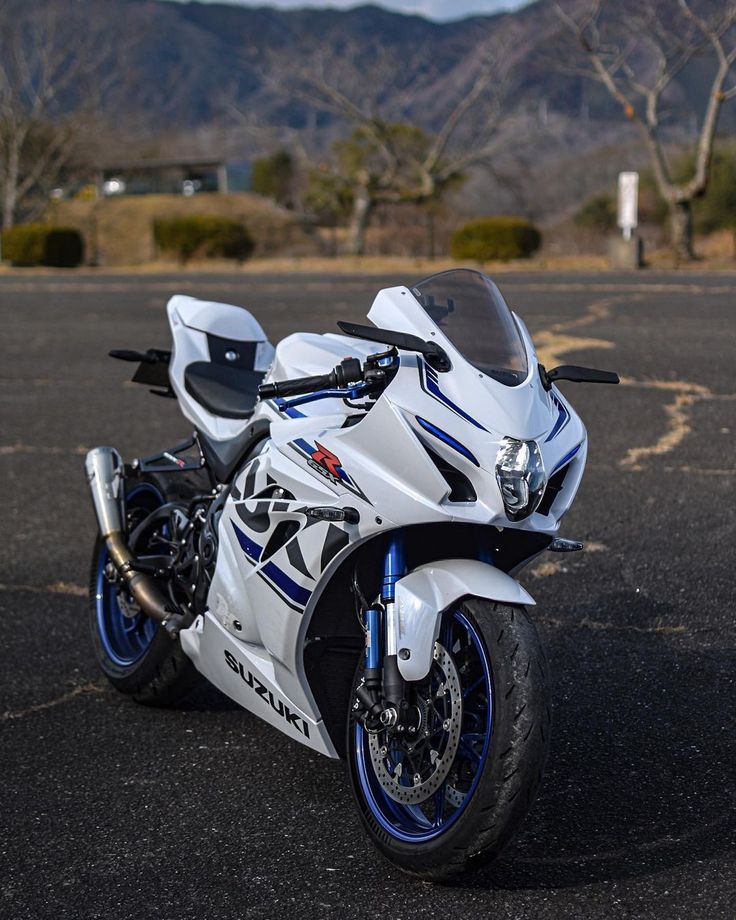 a white and blue motorcycle parked in a parking lot with mountains in the back ground