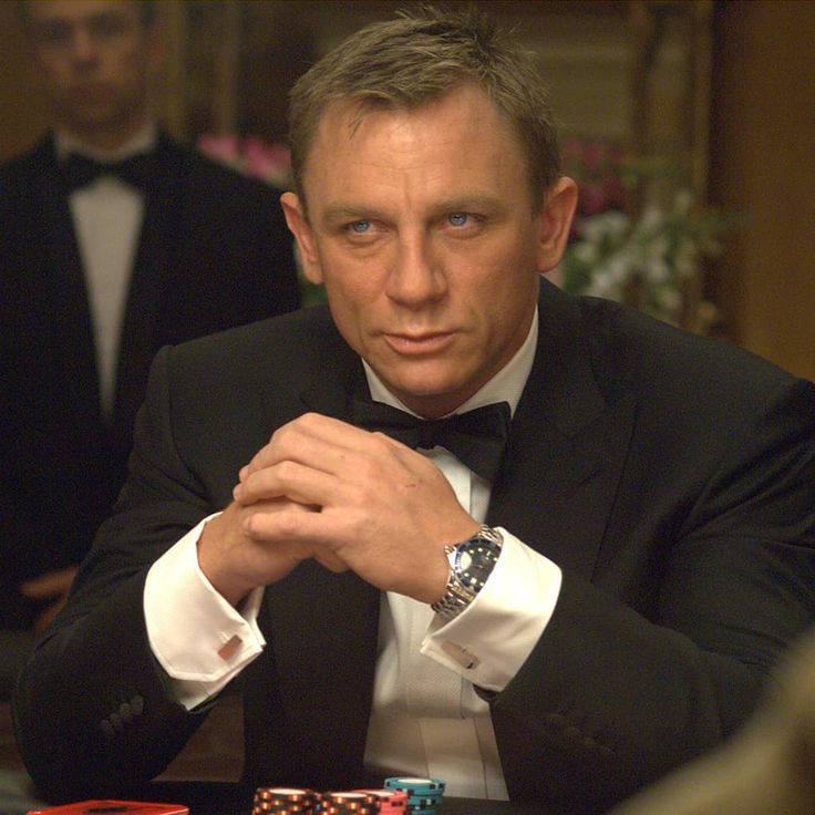 a man in a tuxedo sitting at a table with casino chips and playing cards