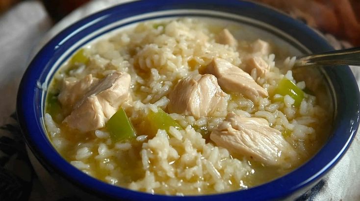 a blue bowl filled with rice and chicken on top of a white table cloth next to bread