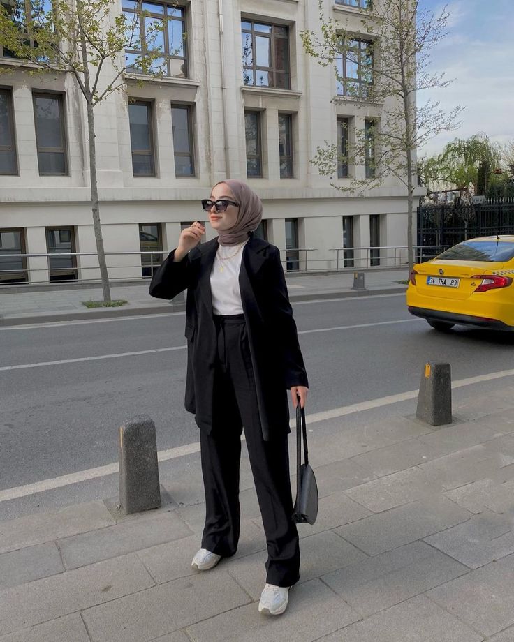 a woman standing on the side of a street talking on a cell phone and holding a purse