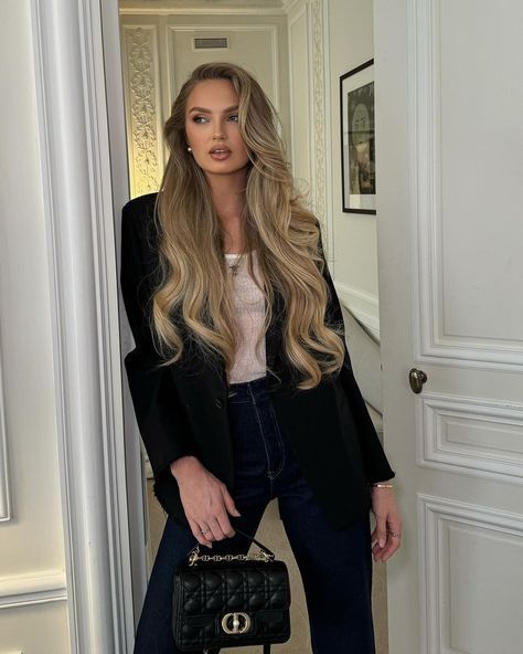 a woman standing next to a doorway holding a black purse and looking at the camera