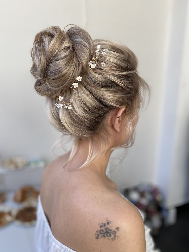 a woman with her hair in a bun and some flowers on her shoulder, looking off to the side