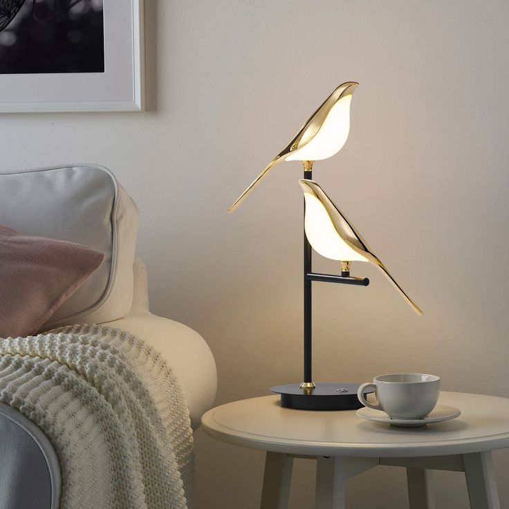 a table lamp that is on top of a white table next to a cup and saucer