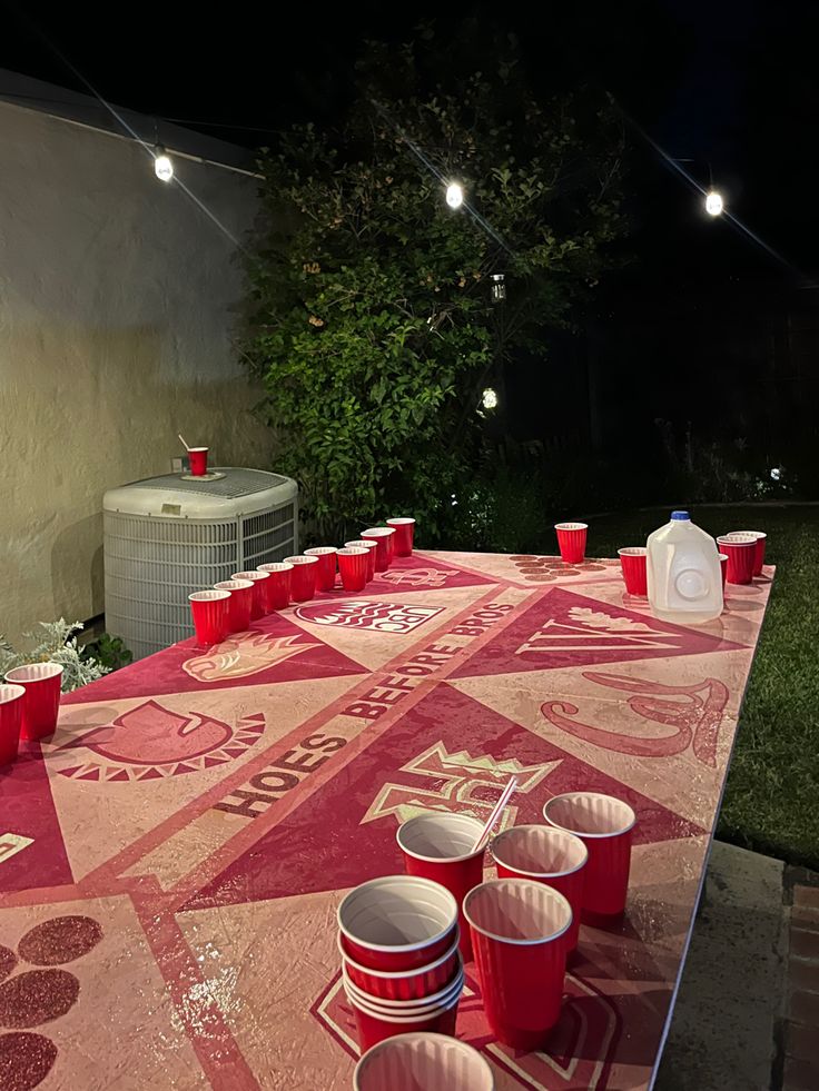 an outdoor table with red cups on it and lights hanging from the ceiling in the background