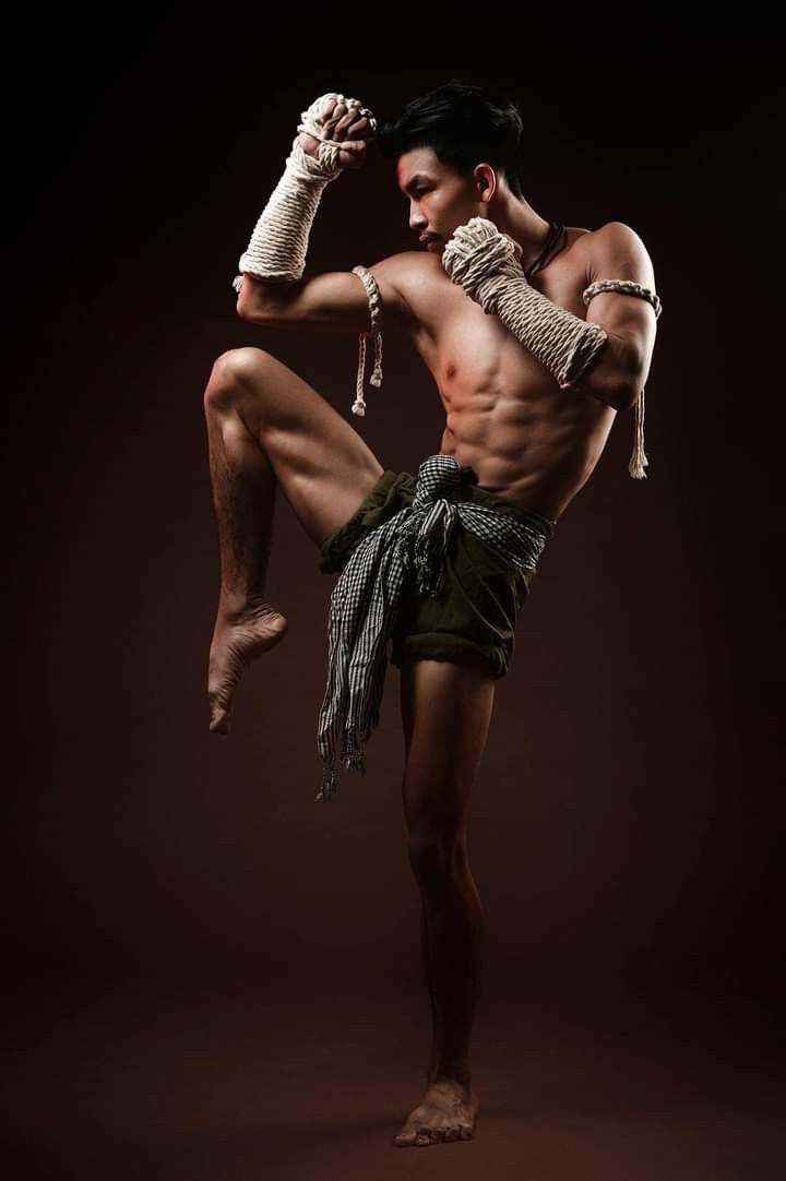 a man with no shirt on is doing a kickbox pose in front of a dark background