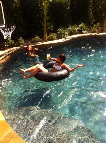 two people floating on an inner tube in a swimming pool with basketball hoop above them