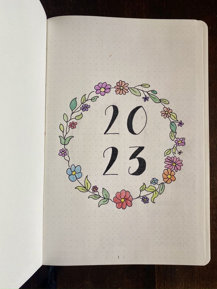 an open notebook with the numbers twenty and three in floral wreaths on top of it