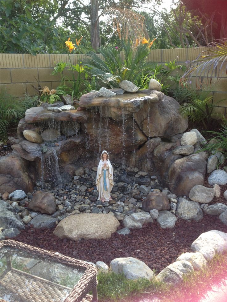 there is a small fountain in the middle of this garden with rocks and plants around it