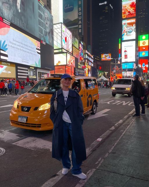 a man standing in the middle of a busy city street at night with taxis and pedestrians