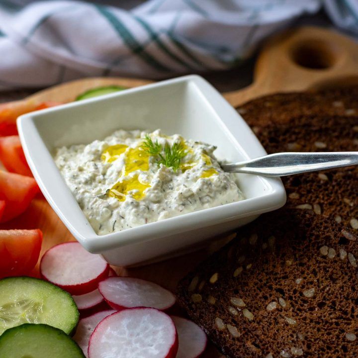 a bowl of dip surrounded by sliced cucumbers and bread