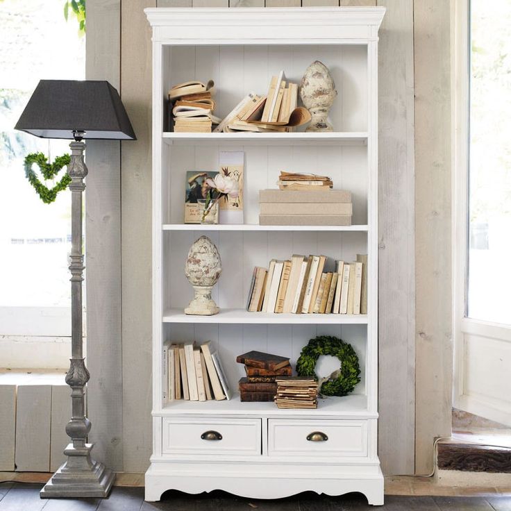 a white bookcase with many books on it and a lamp in the corner next to it