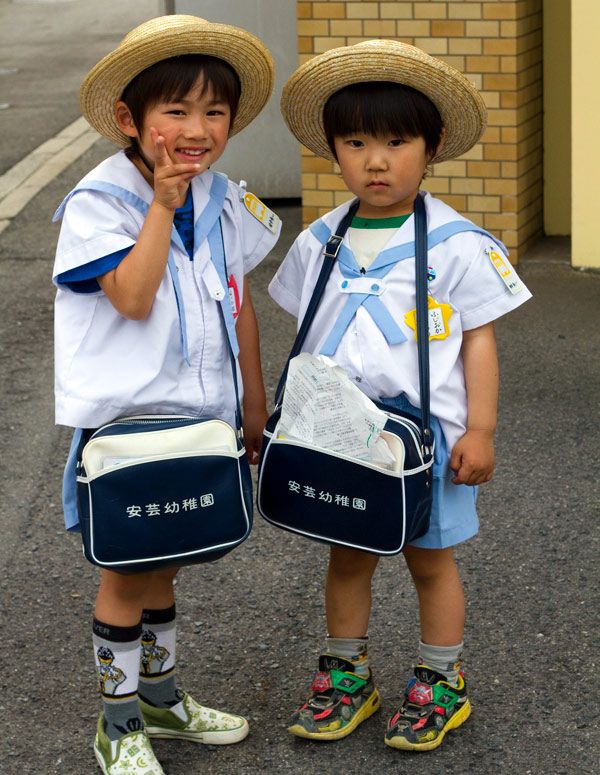 two young children wearing hats and backpacks standing next to each other on the street