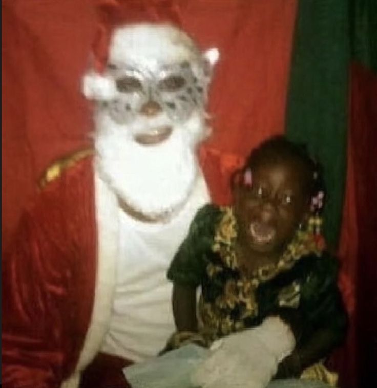 a child is sitting in front of a man dressed as santa claus and wearing a mask