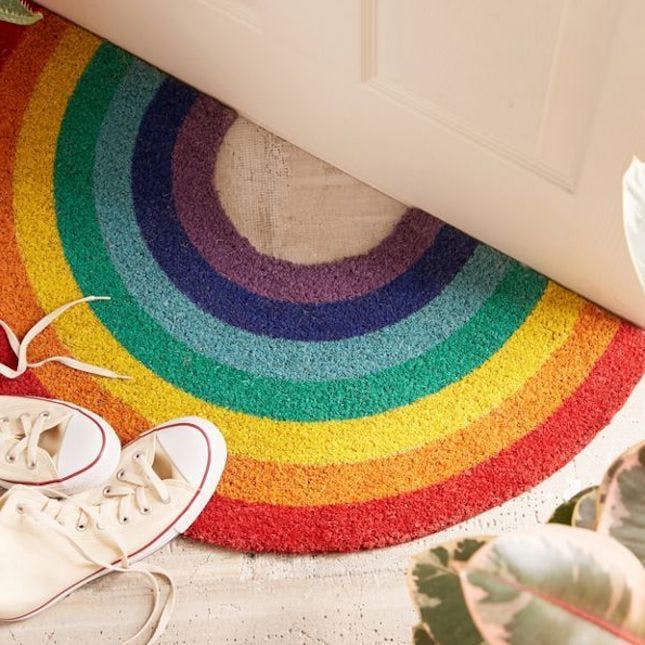 a pair of white tennis shoes sitting on top of a rainbow rug next to a door