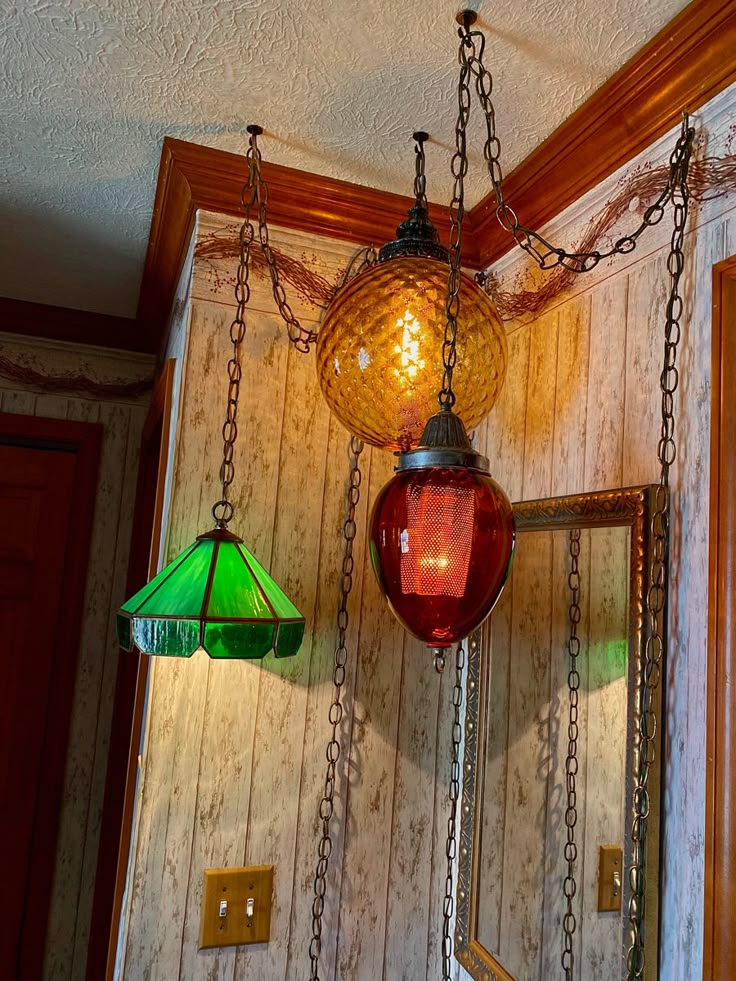 two lamps hanging from chains in a room with wood paneling and green lamp shades