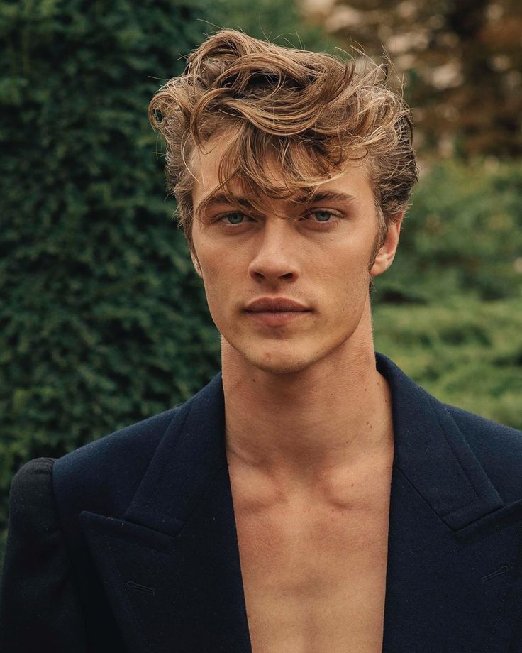 a young man with curly hair and no shirt is standing in front of some bushes