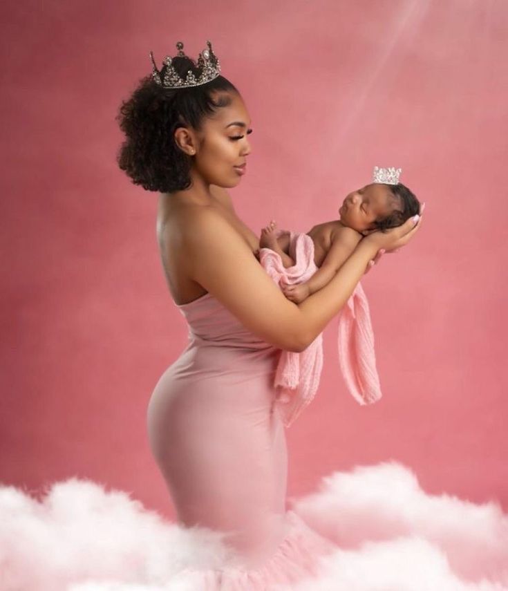 a woman in a pink dress holding a baby wearing a tiara on her head