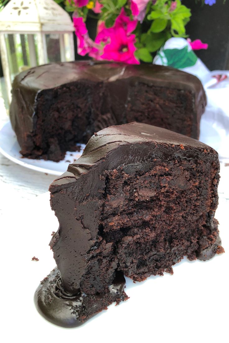 a piece of chocolate cake sitting on top of a white plate next to a vase with flowers