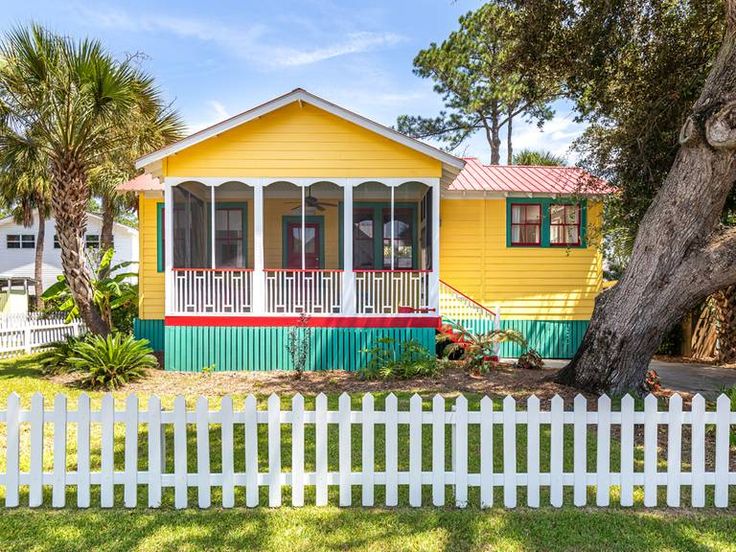 a yellow house with green trim and white picket fence