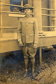 an old photo of a man in uniform standing next to a fence and holding a cane