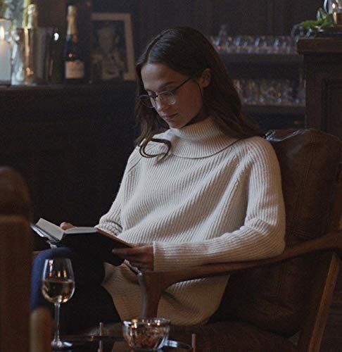 a woman is sitting in a chair reading a book and drinking wine on the table