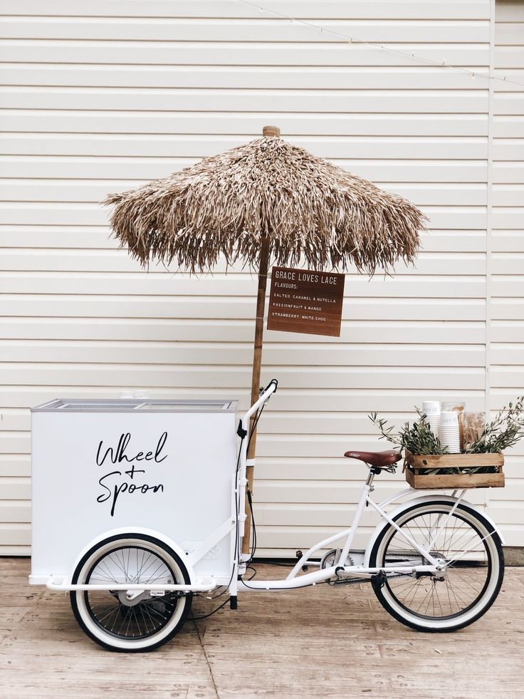 an ice cream cart with a straw umbrella on the back is parked in front of a building