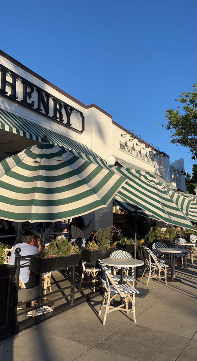 people sitting at tables under umbrellas outside an eatery with green and white striped awning