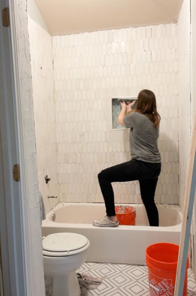 a woman is standing on the edge of a bathtub in front of a toilet