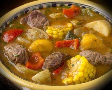 a yellow bowl filled with meat and vegetables on top of a table next to a loaf of bread