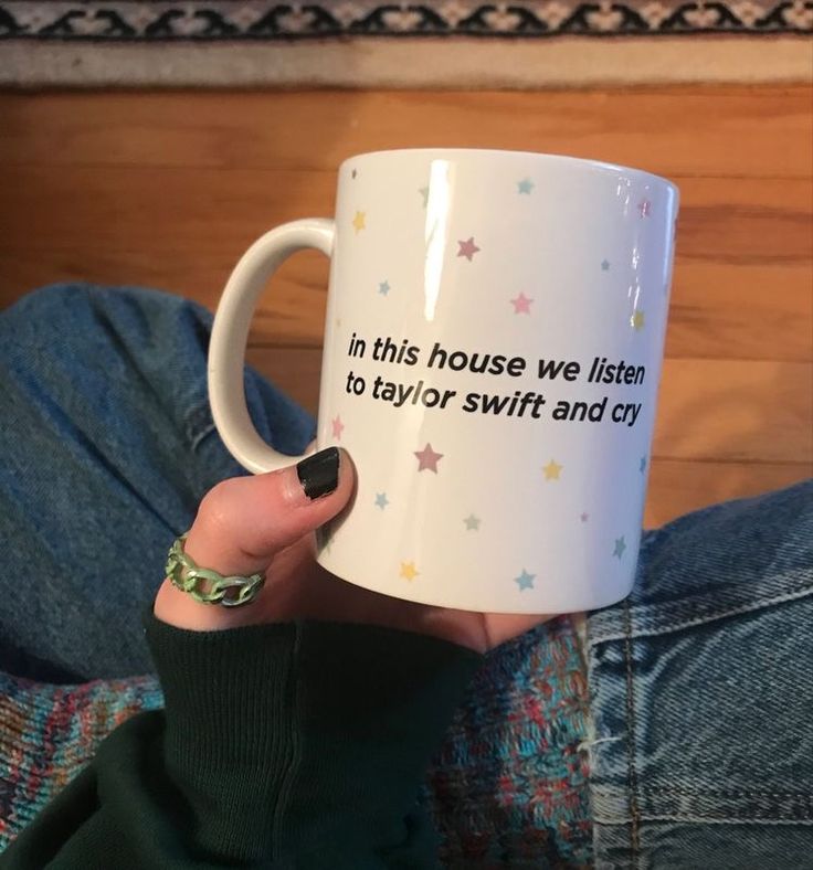 a woman is holding a coffee mug that says in this house we listen to taylor swift and cry