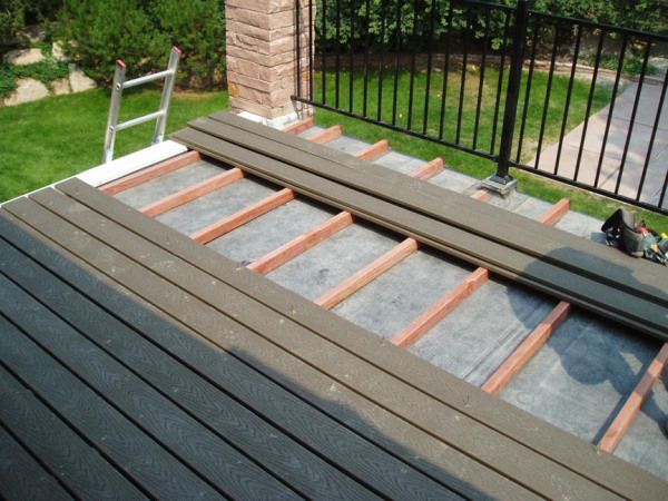 a cat sitting on top of a wooden deck next to a black fence and green grass