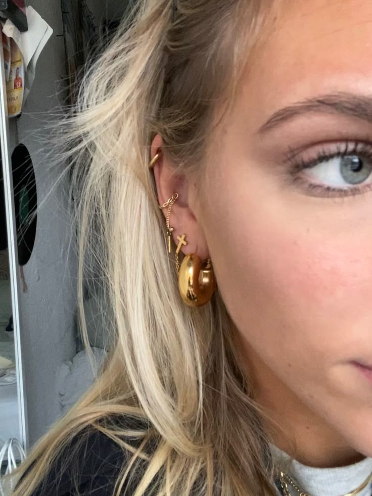 a close up of a person wearing gold earring and necklace with hair in the background