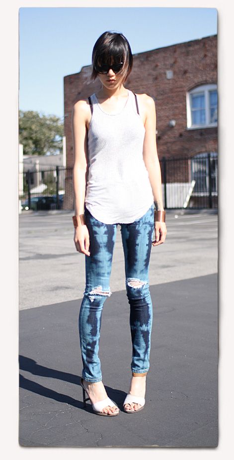 a woman standing in the middle of a parking lot wearing ripped jeans and white tank top