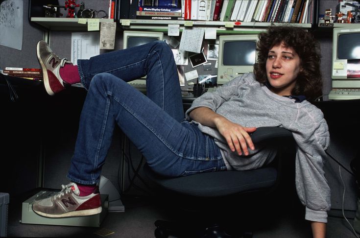 a woman sitting in an office chair with her feet up on the desk and looking at the camera