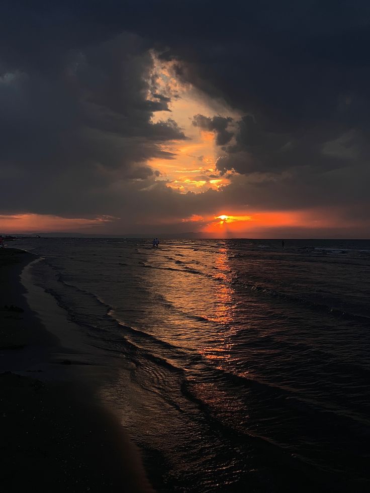 the sun is setting over the ocean with dark clouds