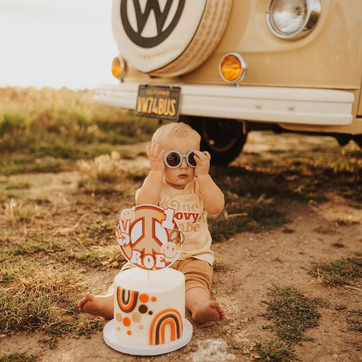 a little boy sitting on the ground next to a cake and a vw bus