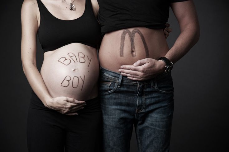 a pregnant woman standing next to a man with the word baby boy written on her belly