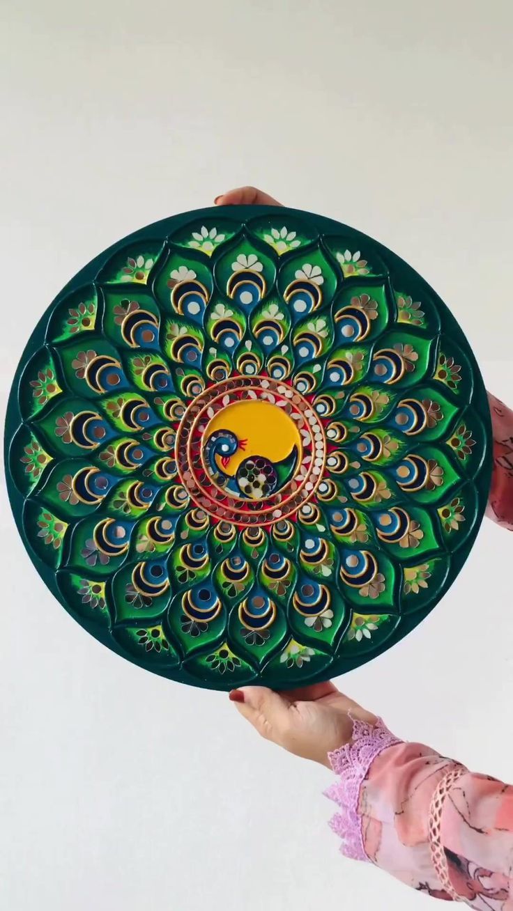 two hands holding a decorative plate in the shape of a peacock