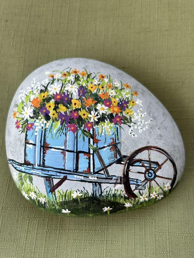 a painted rock sitting on top of a green cloth covered ground with flowers in a wagon