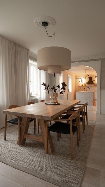 a dining room table and chairs with a lamp hanging over it's head in front of a large window