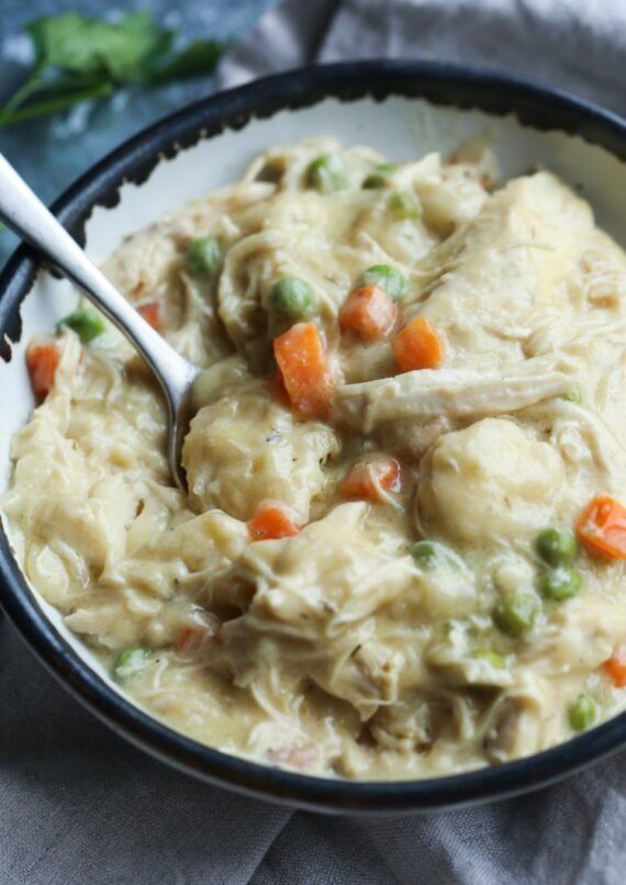 a bowl filled with chicken and dumplings on top of a blue cloth next to a spoon