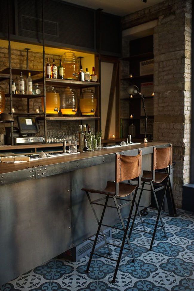 two bar stools sit in front of an empty bar with bottles on the shelves