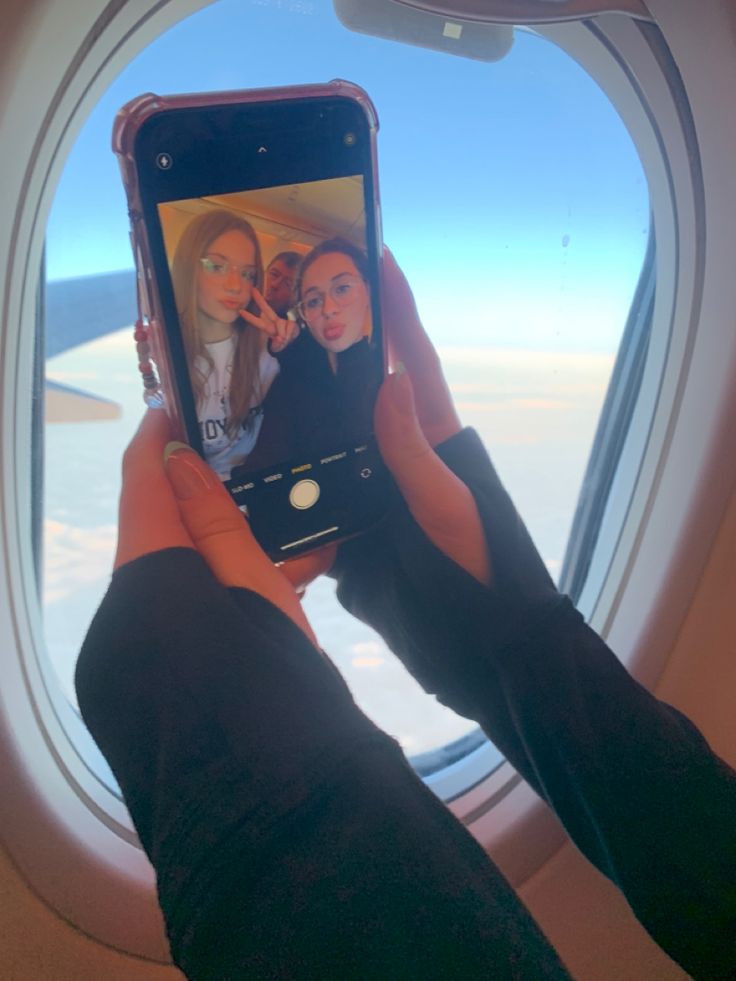 a woman taking a selfie with her cell phone in front of an airplane window